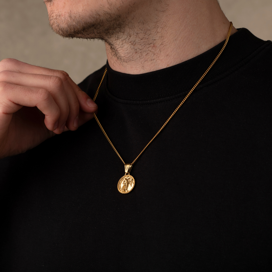 Man wearing a gold necklace with a pendant against a neutral background