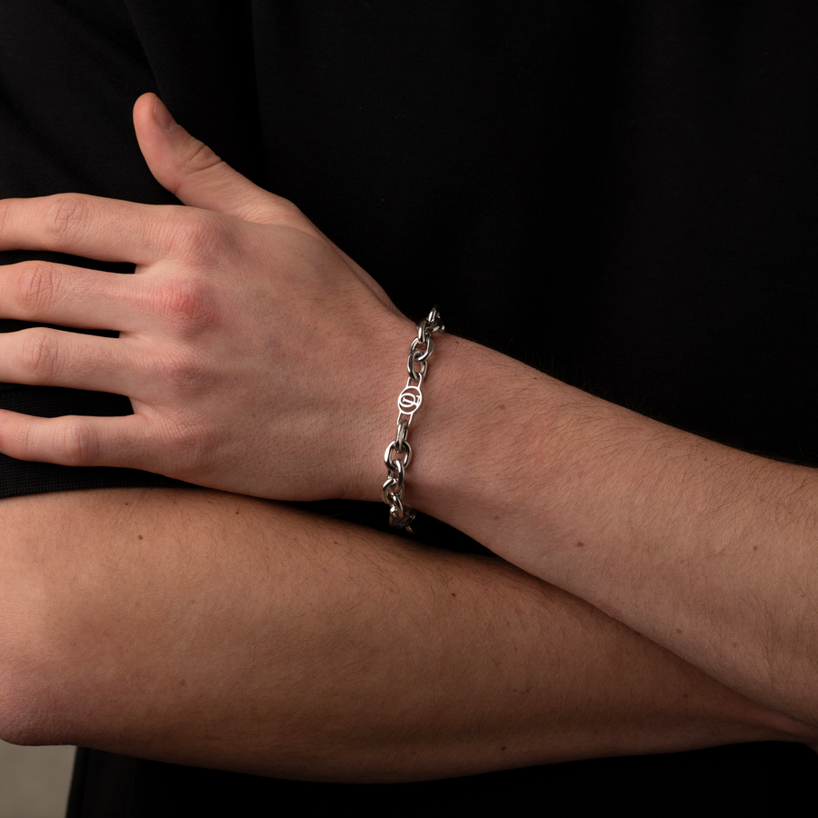 Person wearing a silver chain bracelet on a neutral background