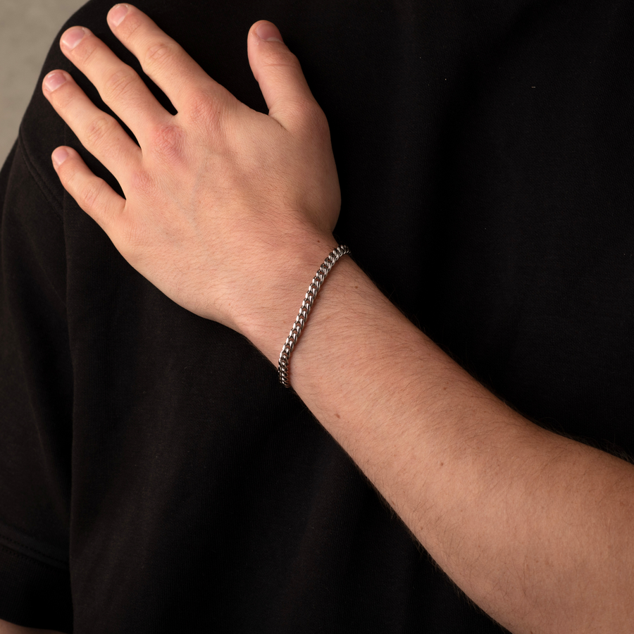 Hand wearing a silver bracelet on a black background