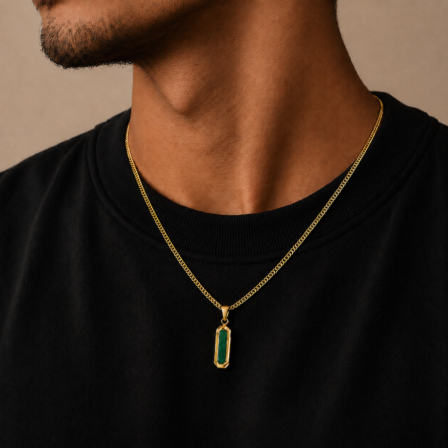 A close-up of a man's neck and chest wearing a gold chain necklace with a vertical rectangular pendant featuring a green inlay, over a black crewneck sweatshirt.