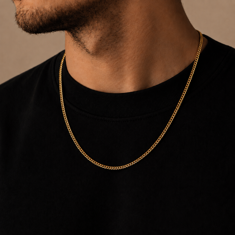 A close-up of a man's neck and lower face wearing a thin gold chain necklace over a black crewneck shirt, set against a warm beige background.