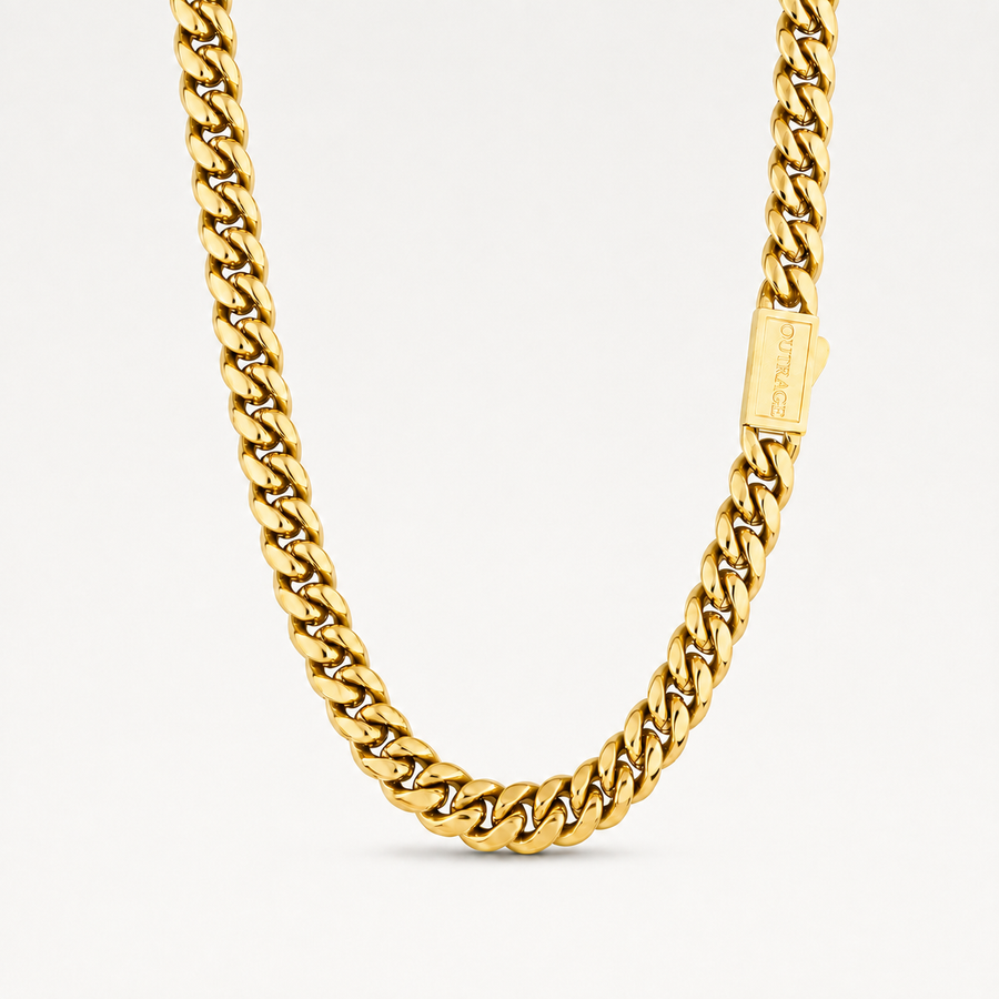 A close-up of a gold Cuban link chain necklace with a rectangular branded tag, photographed against a clean white background.