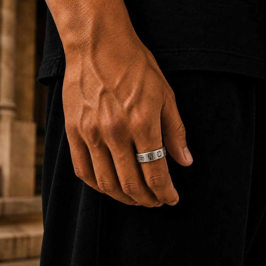 A close-up of a man's hand wearing a silver band ring with repeating interlocking circle motifs, set against a dark shirt and blurred stone background.