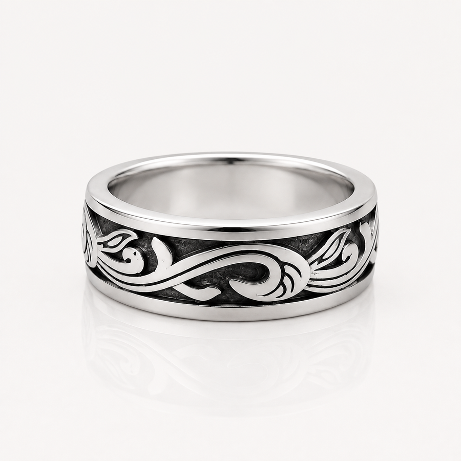 A silver band ring with a polished finish and an engraved black scrollwork pattern, shown on a clean white background with a soft reflection.