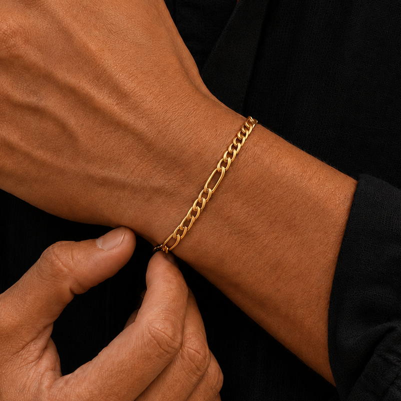 A close-up of a man's wrist wearing a gold chain link bracelet, with his other hand resting on his chest. He is wearing a black button-down shirt.