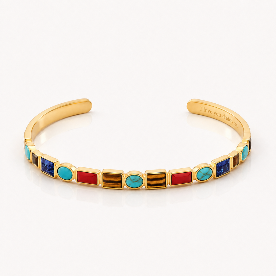 A gold cuff bracelet featuring a row of colorful rectangular and oval bezel-set stones in red, turquoise, blue, and brown, displayed on a clean white background.