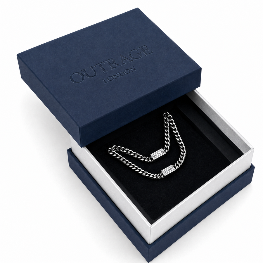 A silver chain necklace with a rectangular plate clasp, presented inside an open navy blue and white OUTFRAGE LONDON gift box.