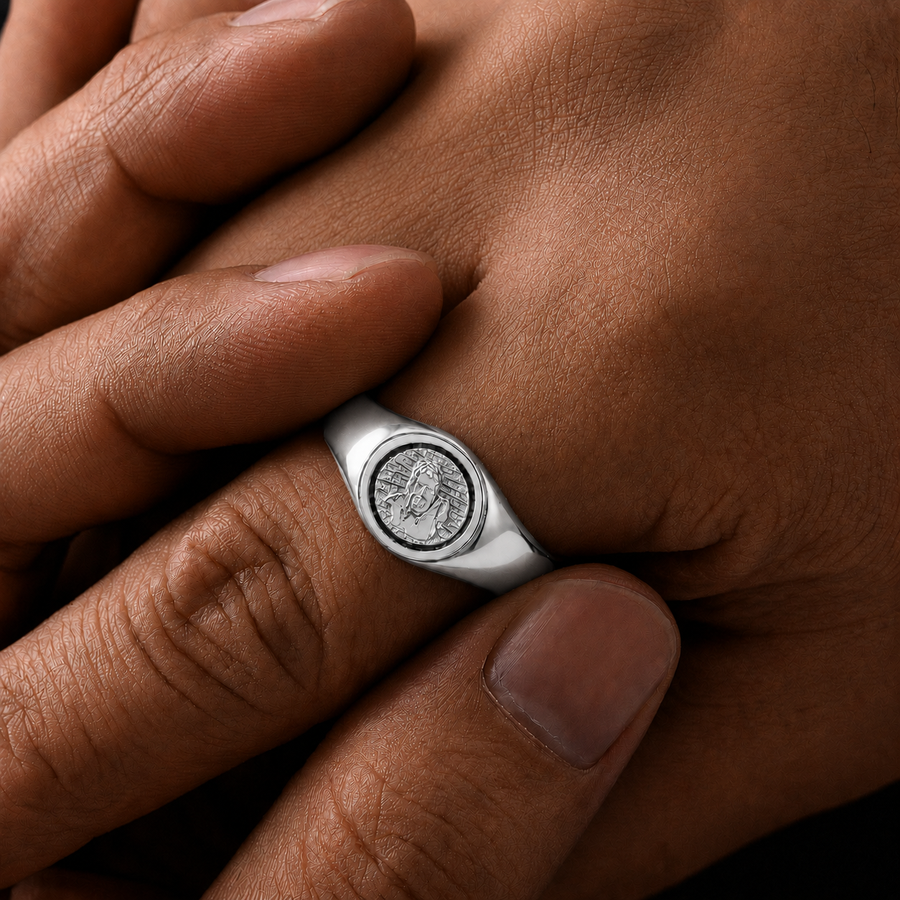A silver signet ring with an engraved circular emblem on the finger, shown in a close-up lifestyle shot against warm skin tones.