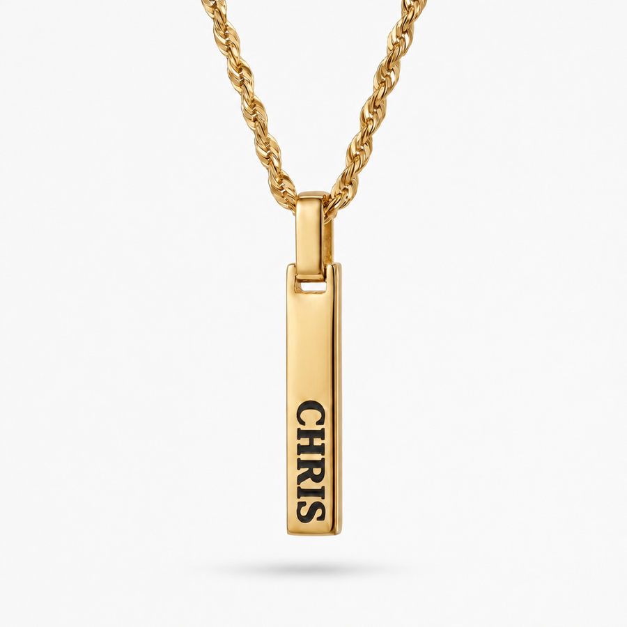 A gold-plated vertical bar pendant necklace engraved with the name 'CHRIS' in black capital letters, suspended from a matching gold rope chain against a light gray background.