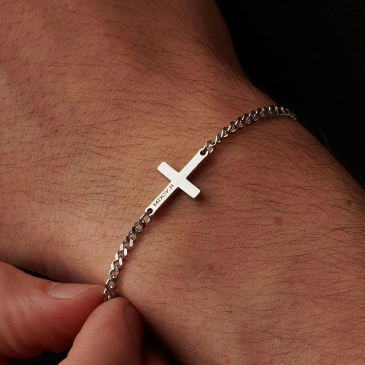 A close-up view of a person's wrist wearing a silver cross-shaped bracelet.