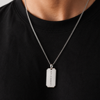 A silver-toned metal pendant necklace worn by a person in a black t-shirt. The pendant is a vertical rectangular tag engraved with the text 'XIV.