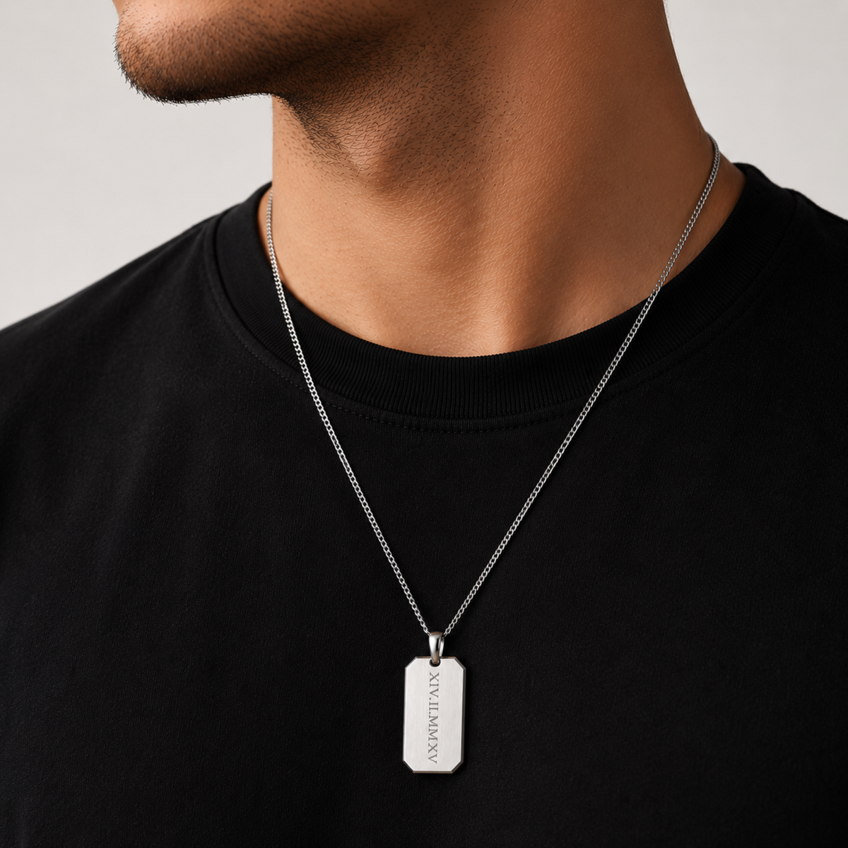 A close-up of a man wearing a silver chain necklace with a rectangular dog tag pendant engraved with the name 'SILVIANOV'.