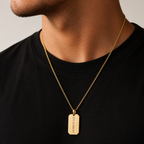A close-up of a man wearing a gold dog tag necklace with the Roman numerals 'IX MILITARE' engraved on it, paired with a black crewneck t-shirt.