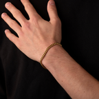 Hand wearing a gold chain bracelet against a black background