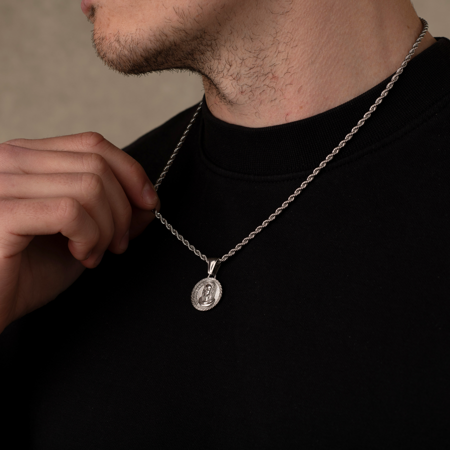 Person wearing a silver necklace with a pendant on a neutral background