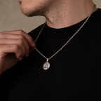 Person wearing a silver necklace with a pendant on a neutral background