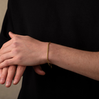 Person wearing a gold bracelet on a plain background