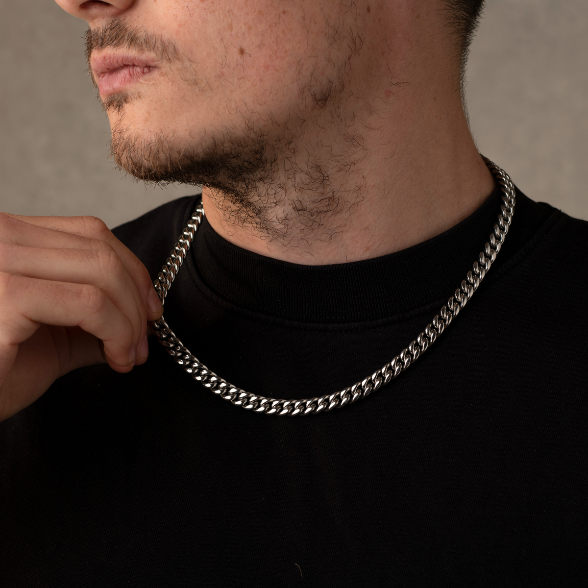Man wearing a silver chain necklace against a neutral background