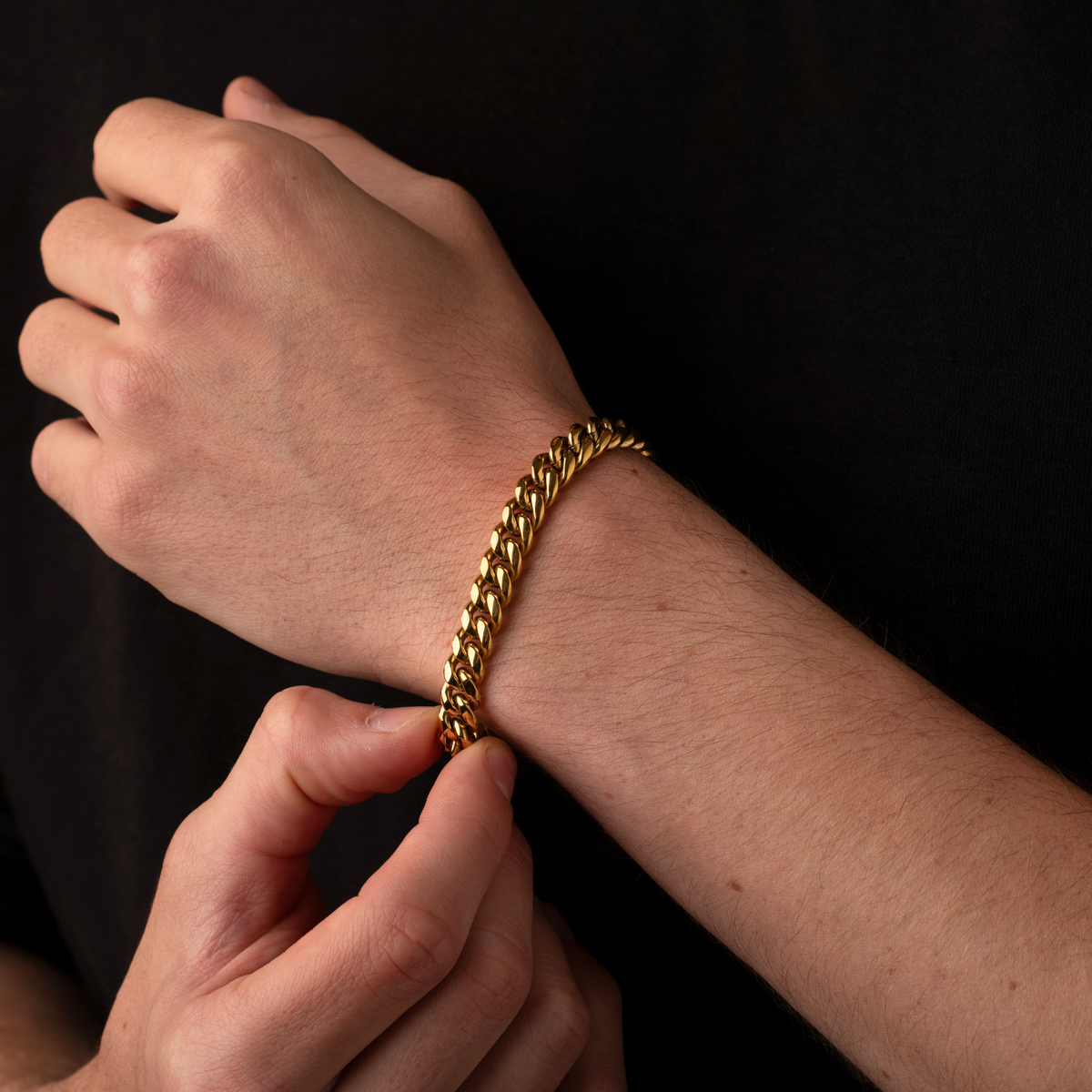 Gold chain bracelet being worn on a wrist against a black background