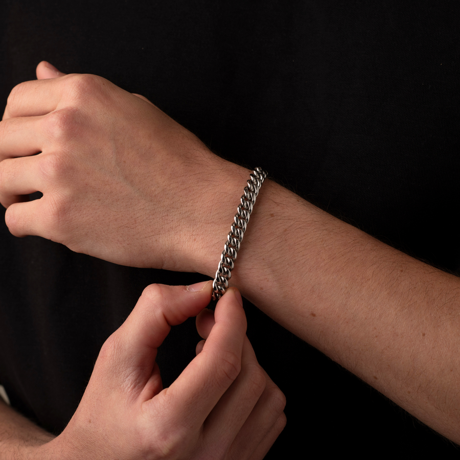 Person adjusting a silver chain bracelet on their wrist against a black background