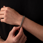 Person adjusting a silver chain bracelet on their wrist against a black background