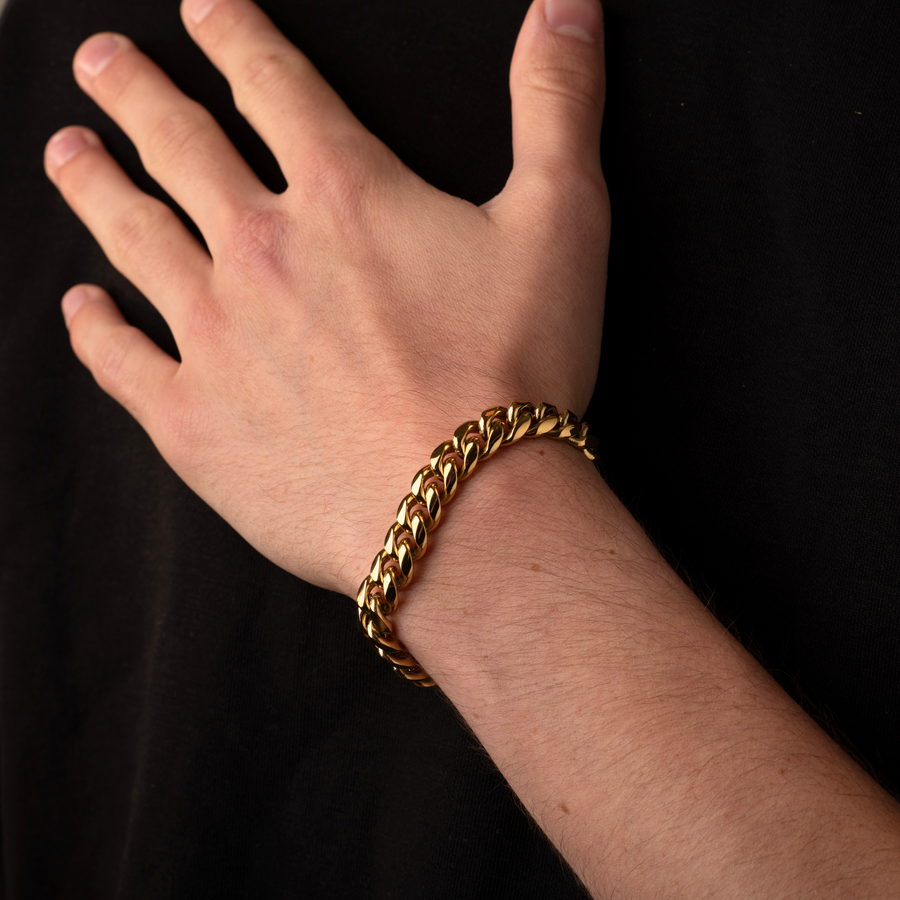 Gold chain bracelet on a person's wrist against a black background