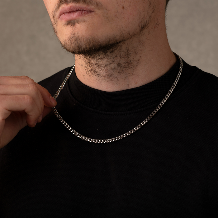 Man adjusting a silver chain necklace against a neutral background