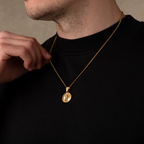 Man wearing a gold necklace with a pendant against a neutral background