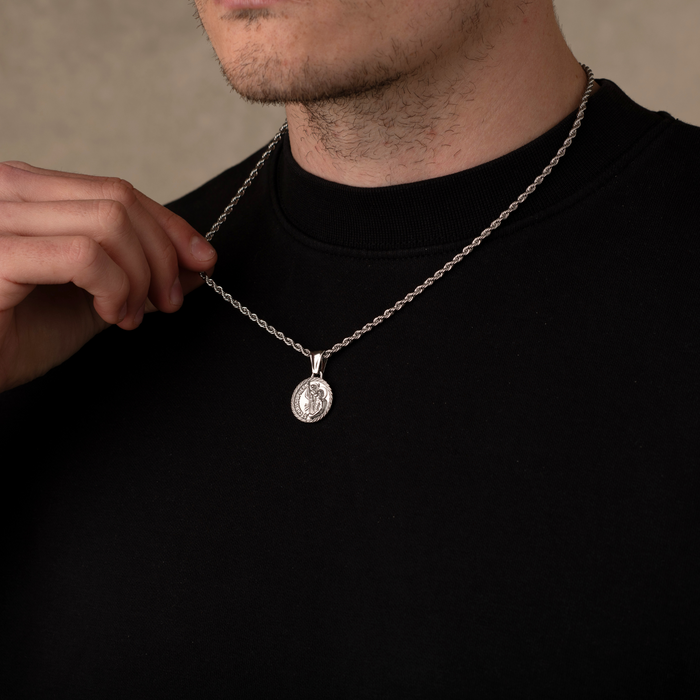 Man wearing a black shirt with a silver necklace featuring a round pendant.