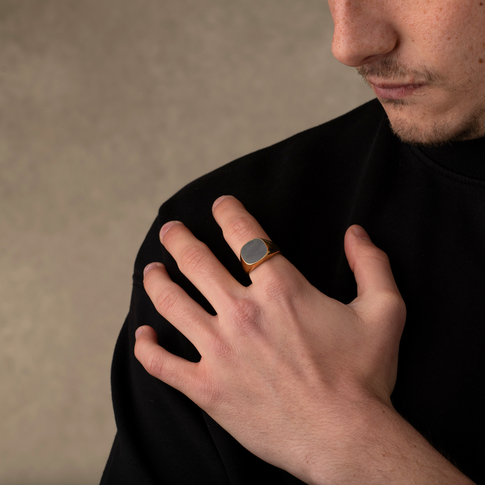 Man wearing a black shirt with a gold ring on his finger against a beige background