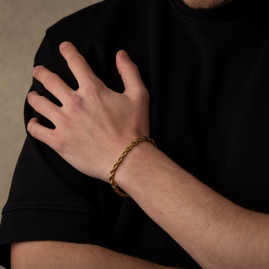 Hand wearing a gold bracelet on a black shirt against a neutral background