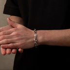 Person wearing a silver chain bracelet on a neutral background