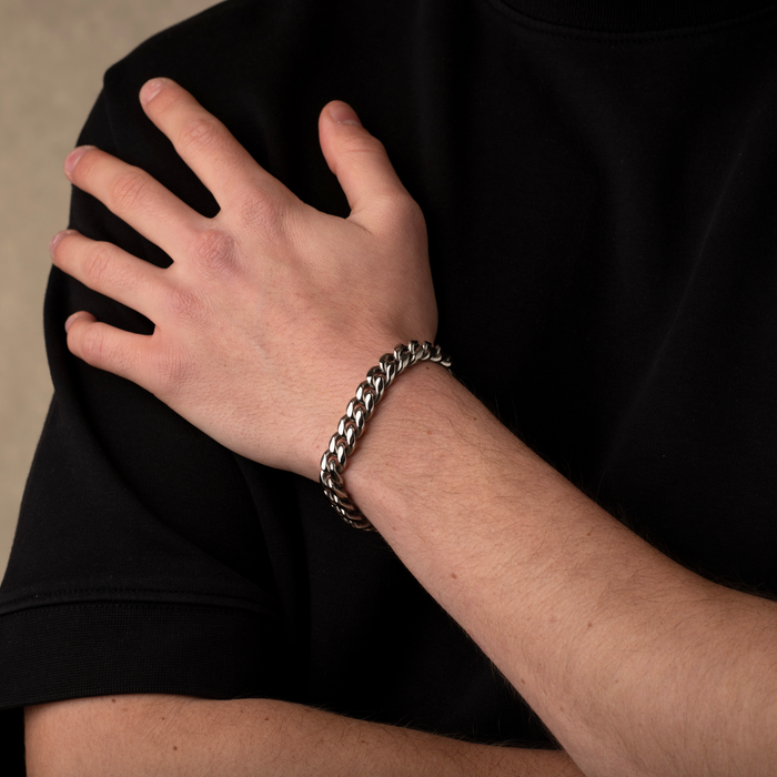 Hand wearing a silver chain bracelet on a black background