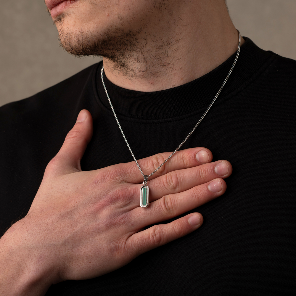 Man wearing a necklace with a green pendant against a neutral background