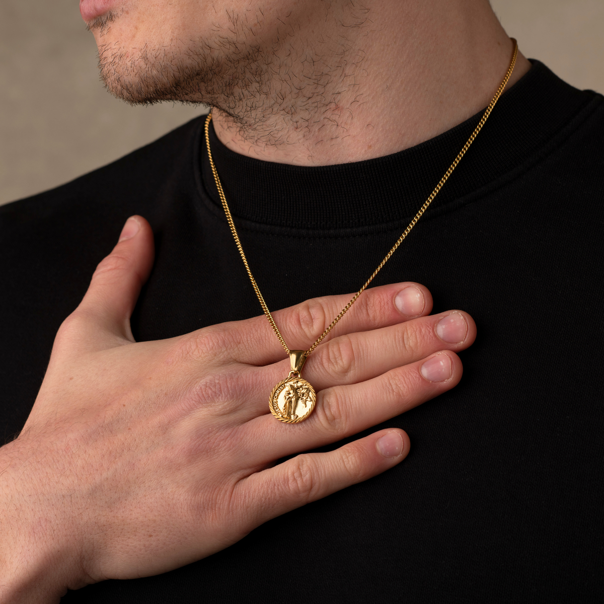 Man wearing a gold necklace with a pendant on a neutral background