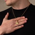 Man wearing a gold necklace with a pendant on a neutral background