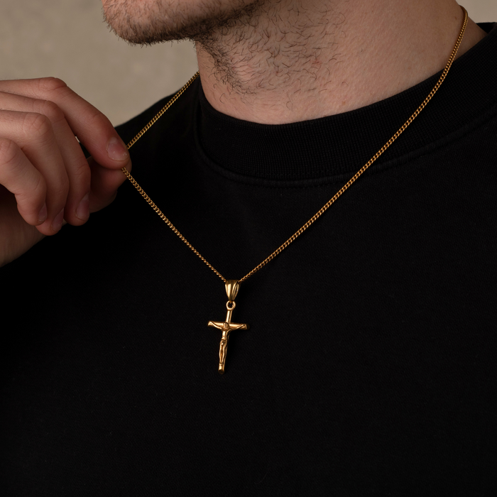 Man wearing a gold necklace with a cross pendant against a neutral background