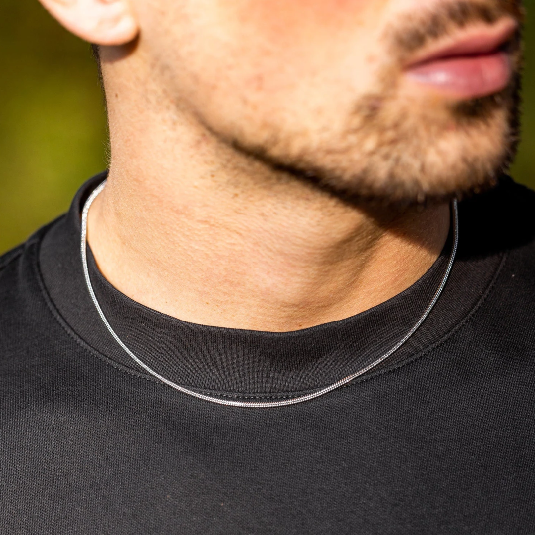 Close-up of a person wearing a black shirt with a thin silver necklace.