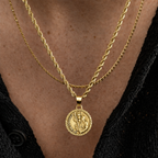 A close-up of a person wearing a double-layered gold necklace with a round Saint Patrick medallion pendant, styled with a black shirt.