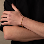 Hand wearing a gold bracelet on a neutral background