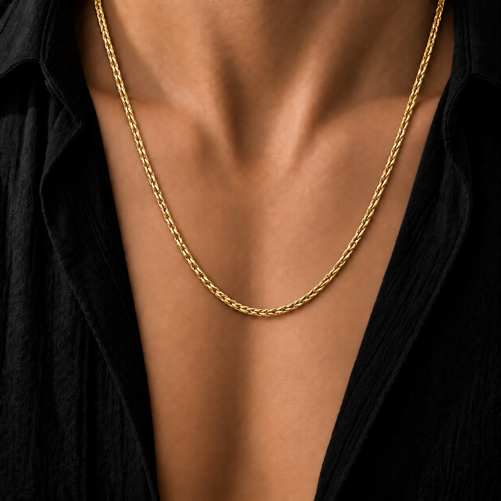 A close-up of a gold Wheat chain necklace worn by a model in a black shirt.