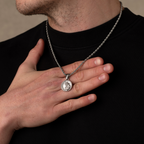 Person holding a silver necklace with a pendant against a neutral background