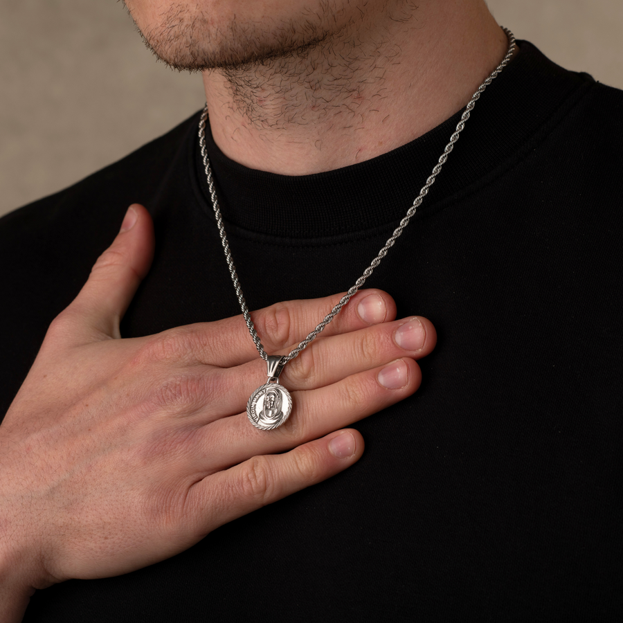 Person wearing a silver necklace with a pendant, holding it with their hand.