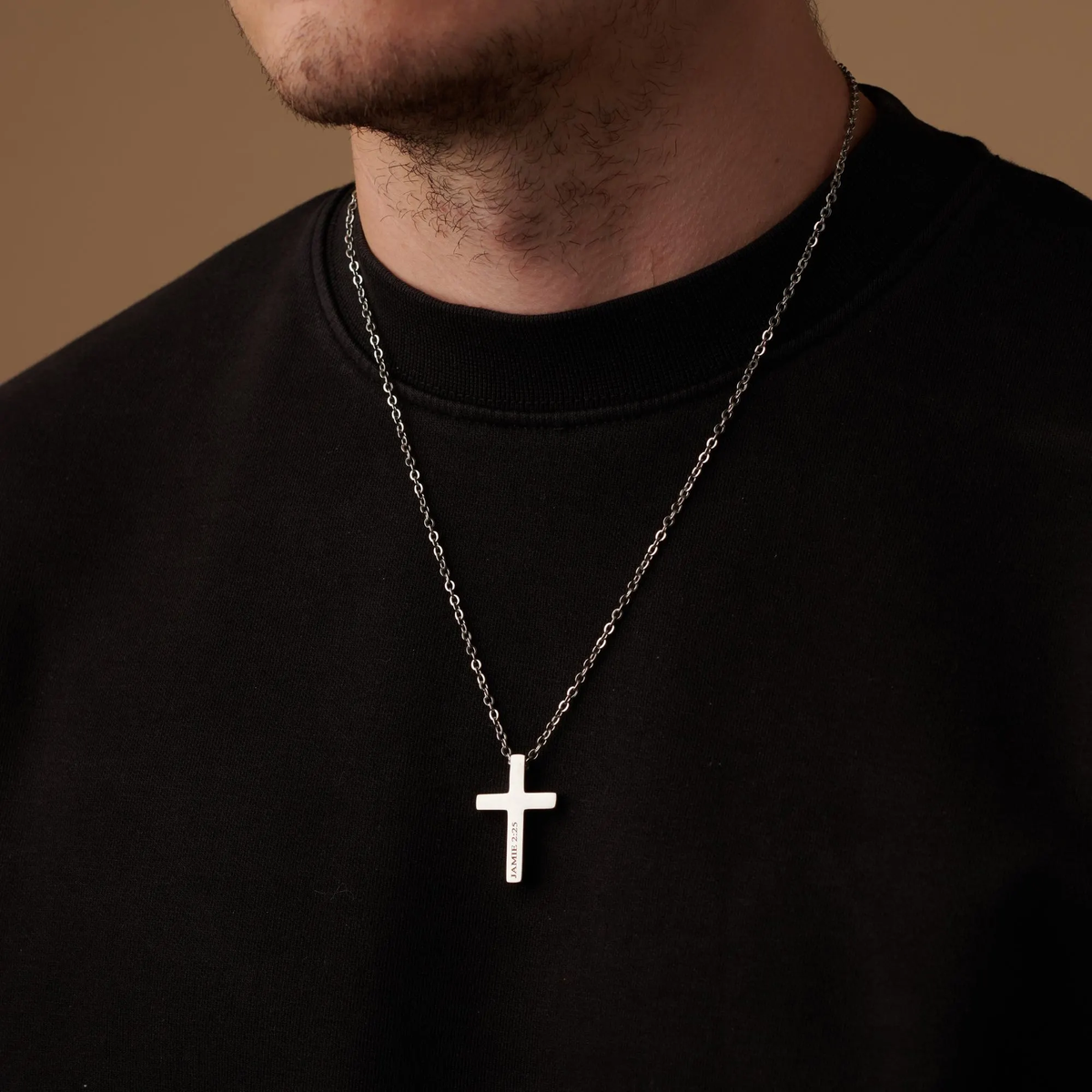 Person wearing a black shirt with a silver cross necklace against a brown background