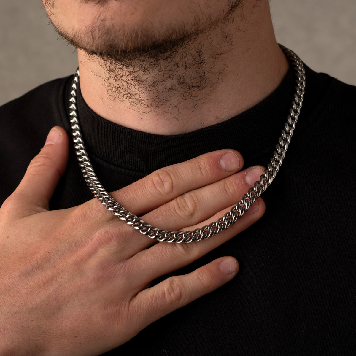 Person wearing a silver chain necklace with a neutral background