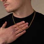 Man wearing a gold chain necklace with a neutral background