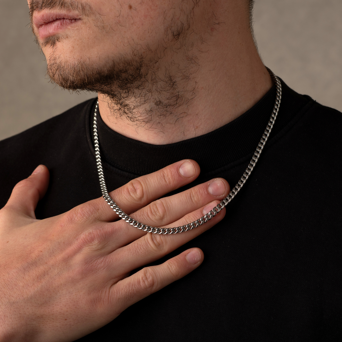 Man wearing a silver chain necklace with a neutral background