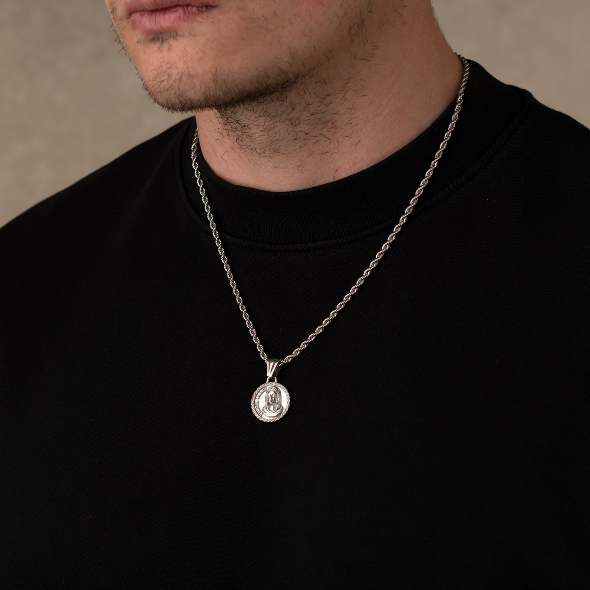 Man wearing a silver necklace with a pendant against a neutral background