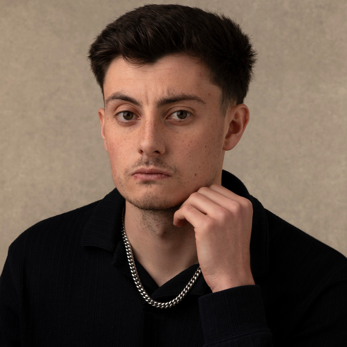 Man wearing a black shirt with a chain necklace against a beige background