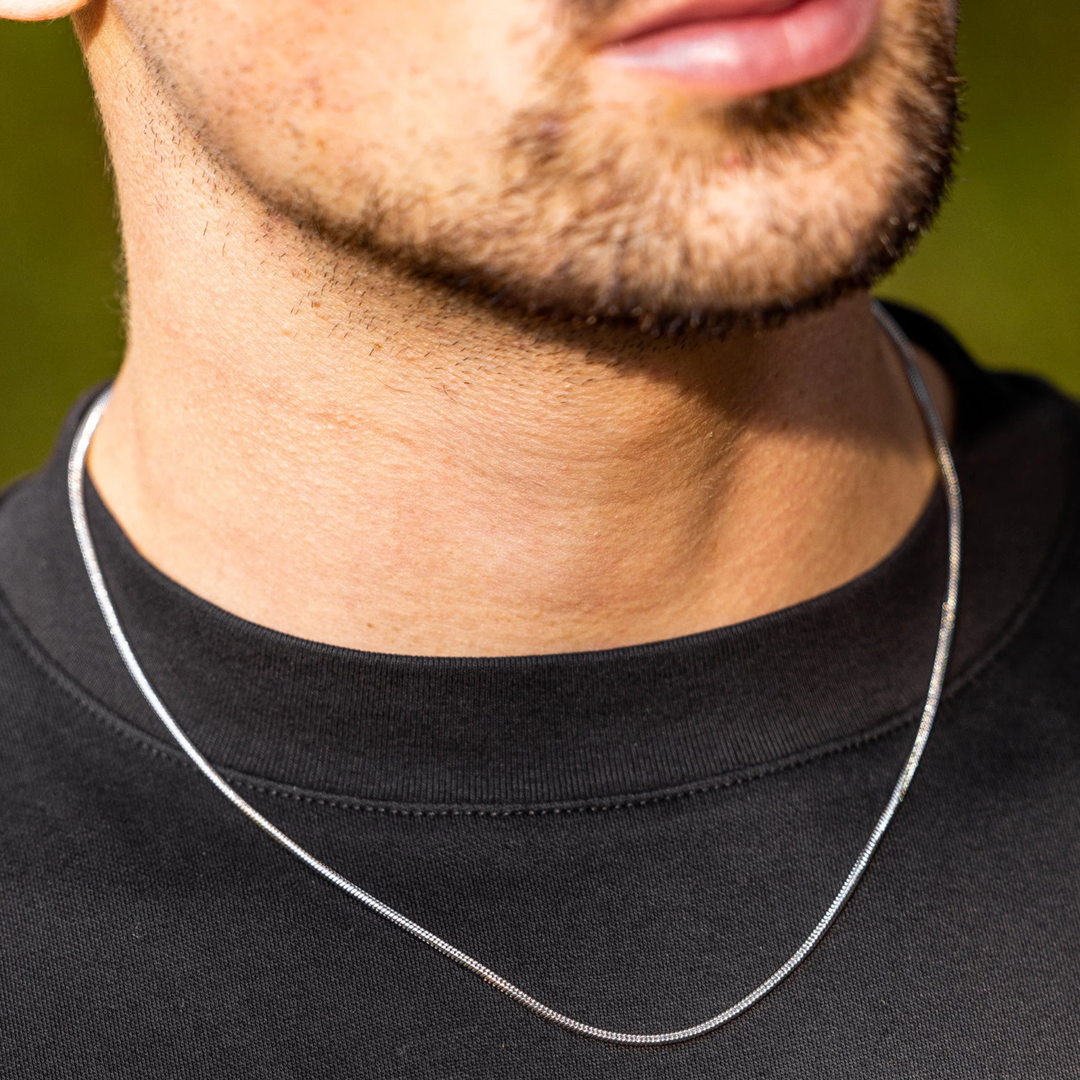 Man wearing a silver necklace against a blurred green background